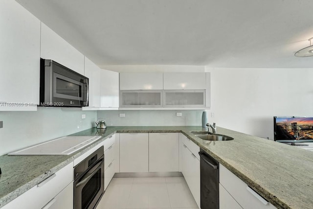 kitchen featuring white cabinets, oven, a sink, light stone countertops, and cooktop