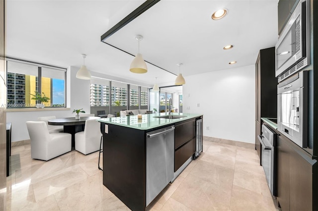 kitchen featuring a center island with sink, sink, stainless steel appliances, and decorative light fixtures