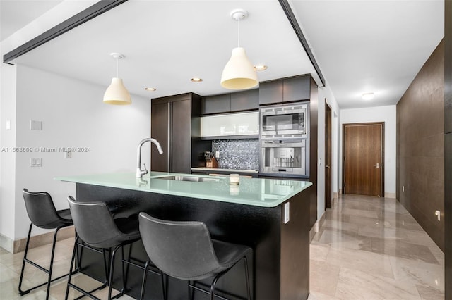 kitchen with dark brown cabinetry, an island with sink, sink, decorative light fixtures, and appliances with stainless steel finishes