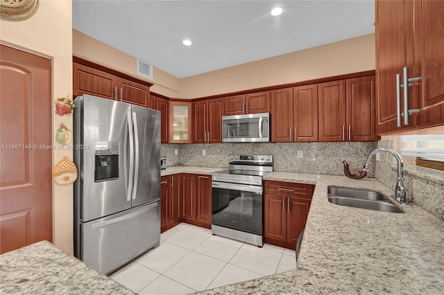 kitchen with appliances with stainless steel finishes, light stone counters, tasteful backsplash, light tile patterned floors, and sink