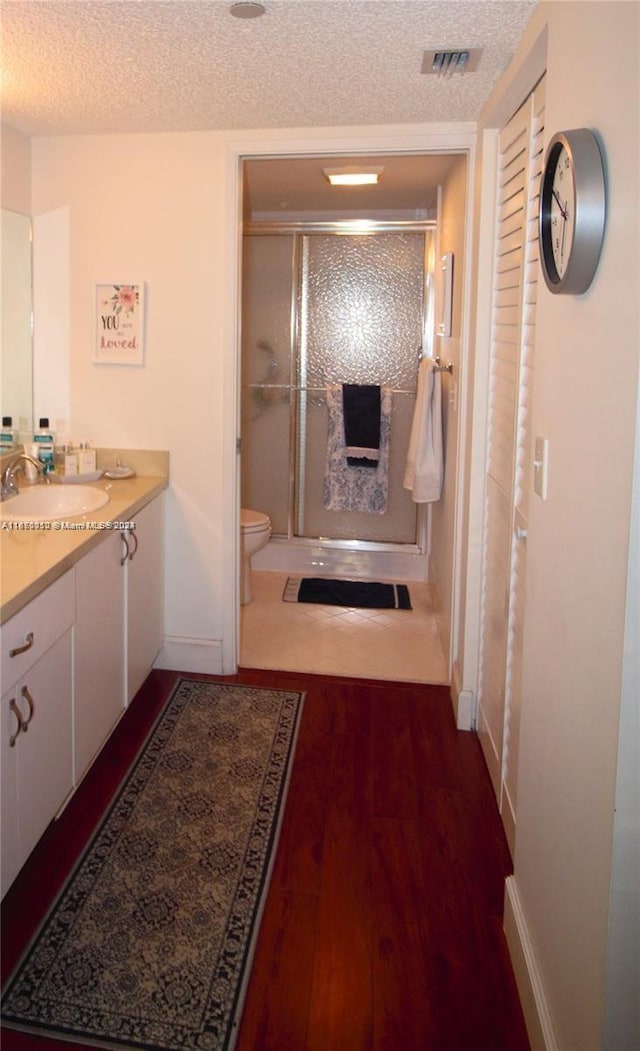 bathroom featuring vanity, an enclosed shower, a textured ceiling, hardwood / wood-style flooring, and toilet