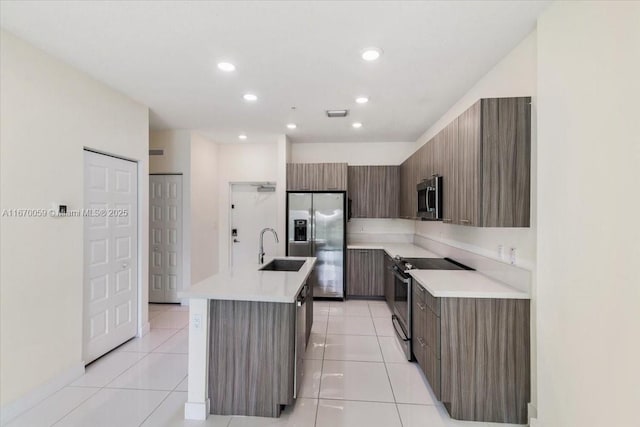 kitchen with sink, light tile patterned floors, an island with sink, and appliances with stainless steel finishes