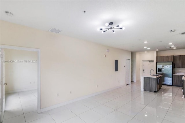 kitchen with a kitchen island with sink, sink, stainless steel refrigerator with ice dispenser, light tile patterned floors, and dark brown cabinetry