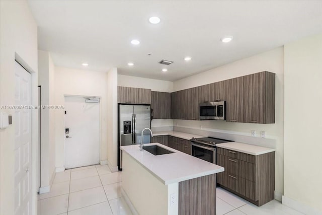 kitchen with dark brown cabinets, stainless steel appliances, sink, a center island with sink, and light tile patterned flooring