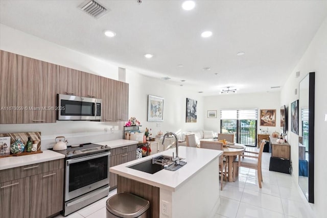 kitchen featuring appliances with stainless steel finishes, light tile patterned floors, a kitchen island with sink, and sink