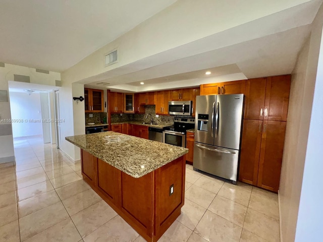 kitchen featuring light stone countertops, sink, a center island, stainless steel appliances, and tasteful backsplash