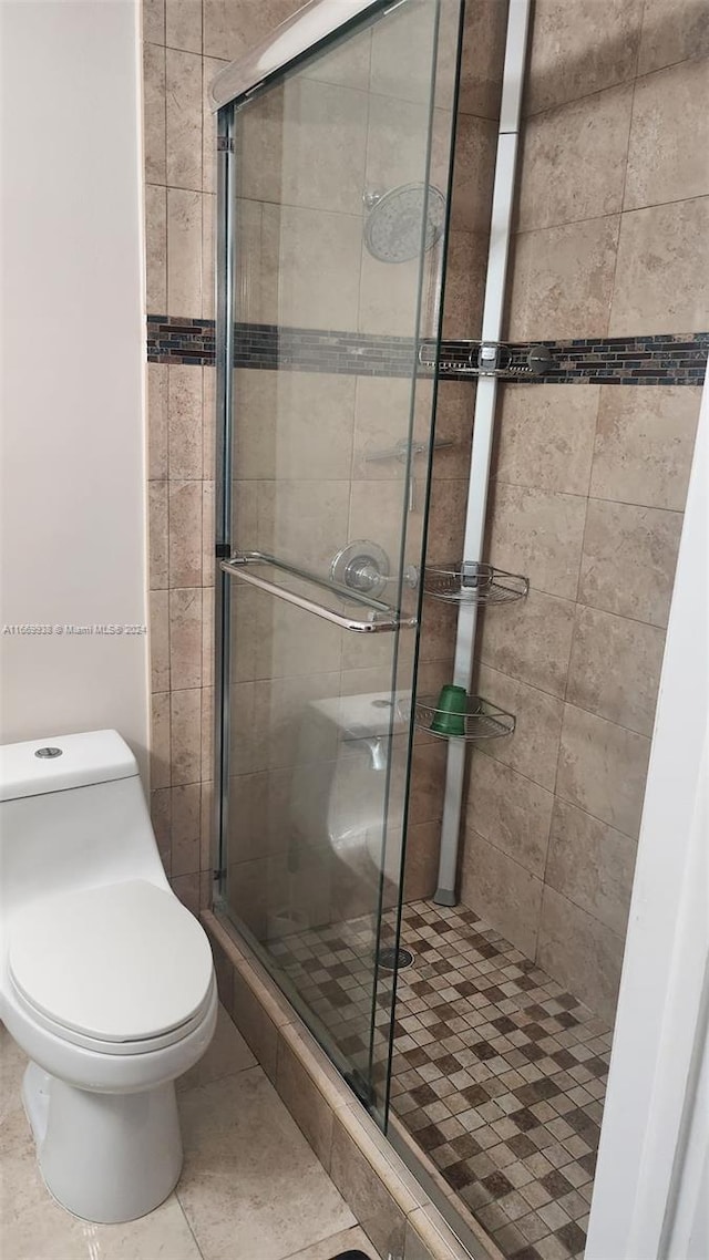 bathroom with tile patterned flooring, a shower with shower door, and toilet