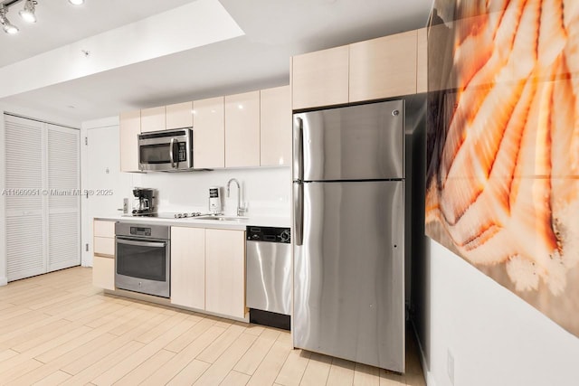 kitchen with modern cabinets, light wood-style flooring, a sink, appliances with stainless steel finishes, and light countertops