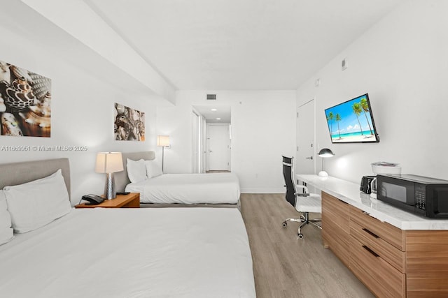 bedroom with light wood-type flooring, baseboards, visible vents, and built in desk