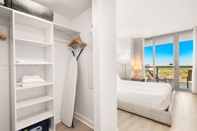 bedroom with access to exterior, floor to ceiling windows, wood finished floors, and baseboards