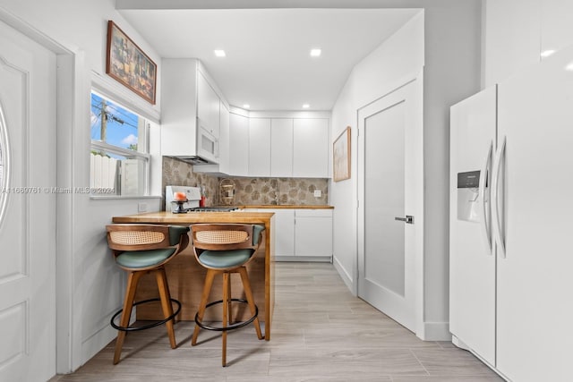 kitchen featuring light wood-type flooring, wood counters, white cabinetry, a kitchen bar, and white appliances