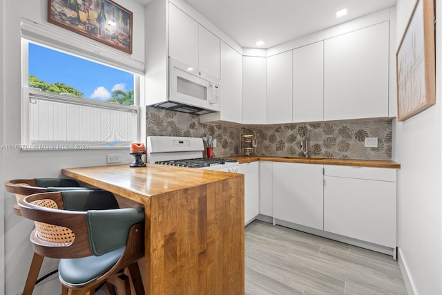 kitchen featuring decorative backsplash, white cabinets, white appliances, kitchen peninsula, and light wood-type flooring