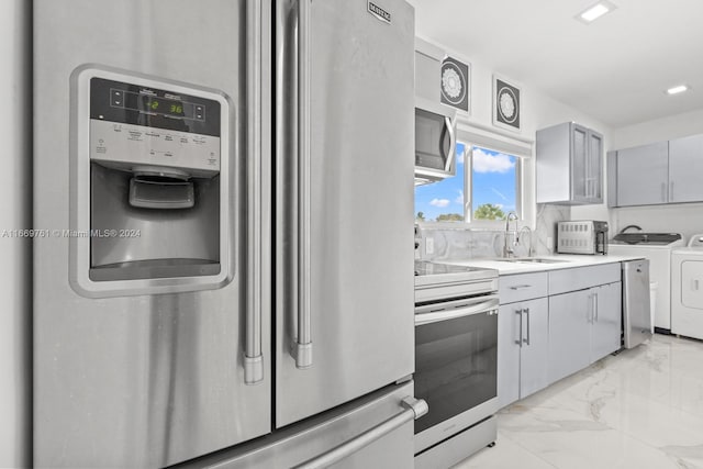 kitchen with sink, appliances with stainless steel finishes, washer and dryer, and gray cabinets