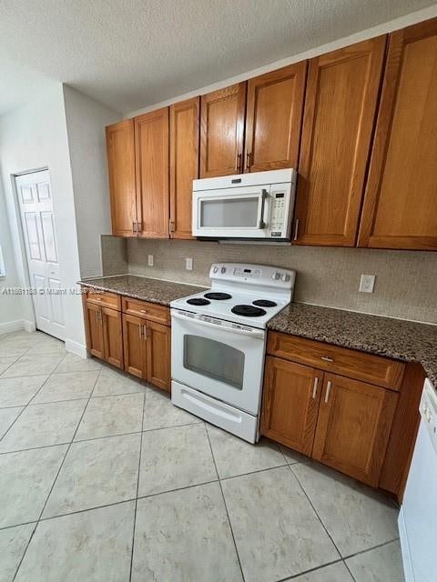 kitchen with dark stone counters, white appliances, a textured ceiling, and light tile patterned floors