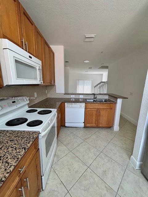 kitchen featuring dark stone countertops, white appliances, kitchen peninsula, a textured ceiling, and sink