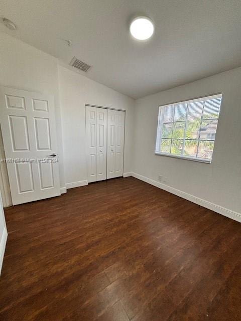 unfurnished bedroom with a closet, dark hardwood / wood-style floors, and vaulted ceiling