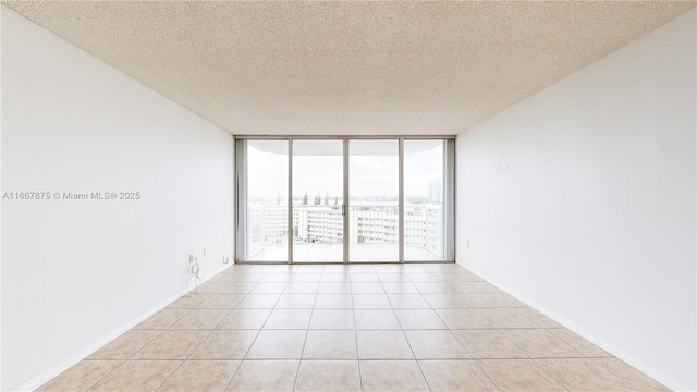 empty room with light tile patterned flooring, a textured ceiling, and a wall of windows