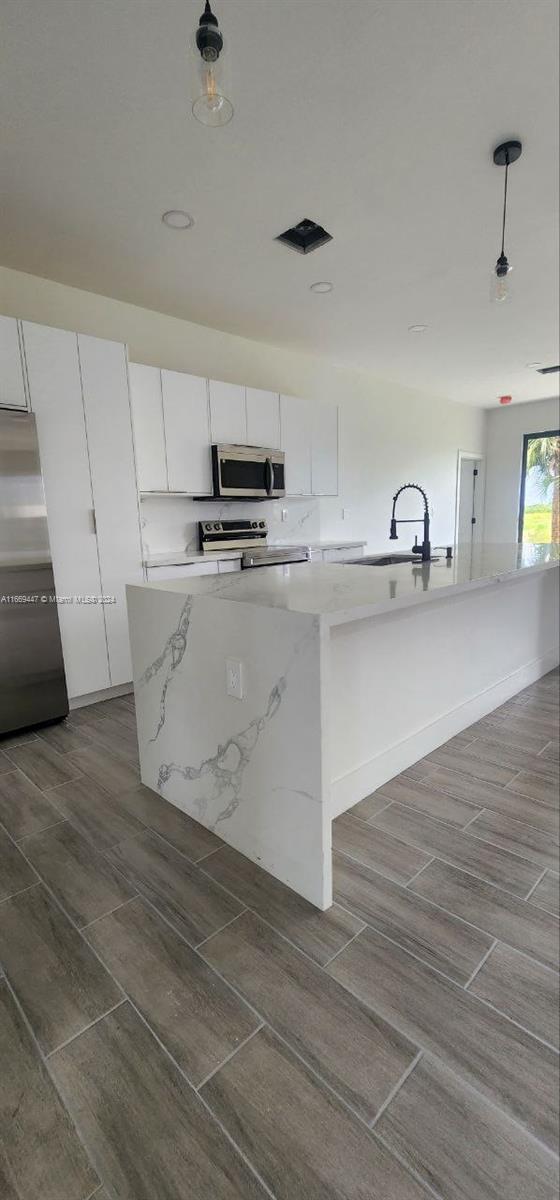 kitchen featuring appliances with stainless steel finishes, sink, an island with sink, and white cabinets