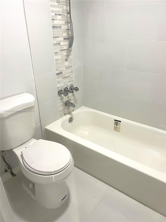 bathroom featuring tile patterned flooring, tiled shower / bath combo, and toilet