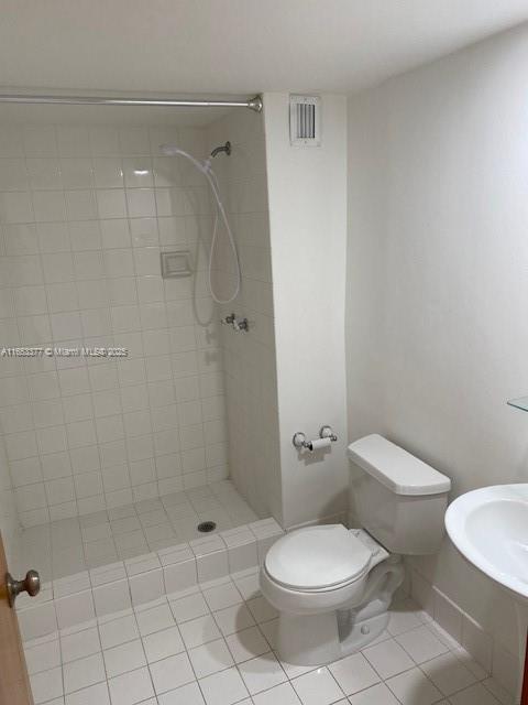 bathroom featuring tile patterned flooring, tiled shower, sink, and toilet