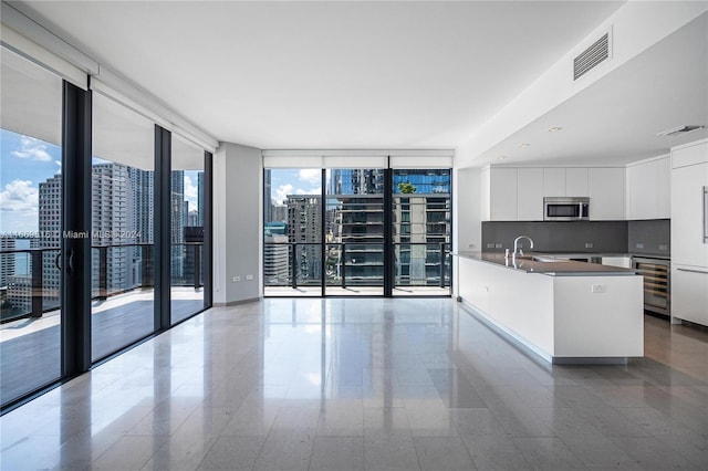 kitchen featuring white cabinetry, plenty of natural light, a kitchen island with sink, and expansive windows