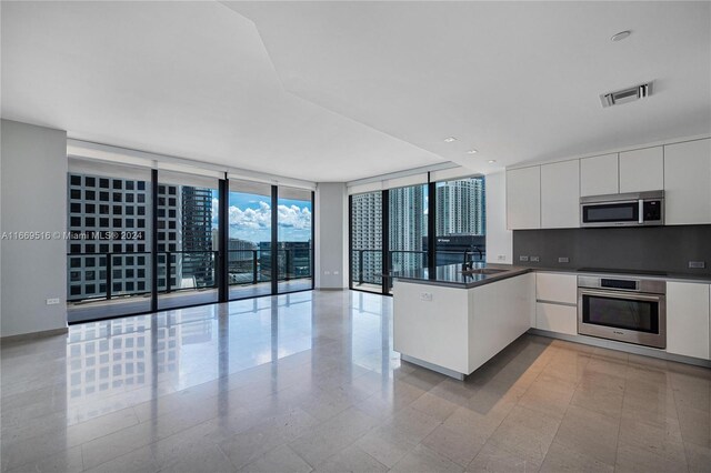 kitchen featuring expansive windows, white cabinets, sink, kitchen peninsula, and stainless steel appliances