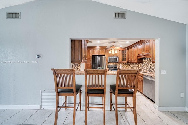 kitchen with light tile patterned flooring, lofted ceiling, kitchen peninsula, appliances with stainless steel finishes, and decorative backsplash