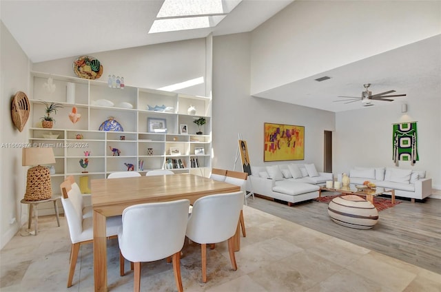 dining area featuring light wood-type flooring, ceiling fan, a skylight, and high vaulted ceiling