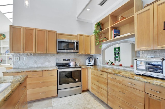 kitchen with appliances with stainless steel finishes, backsplash, light stone countertops, and light tile patterned floors