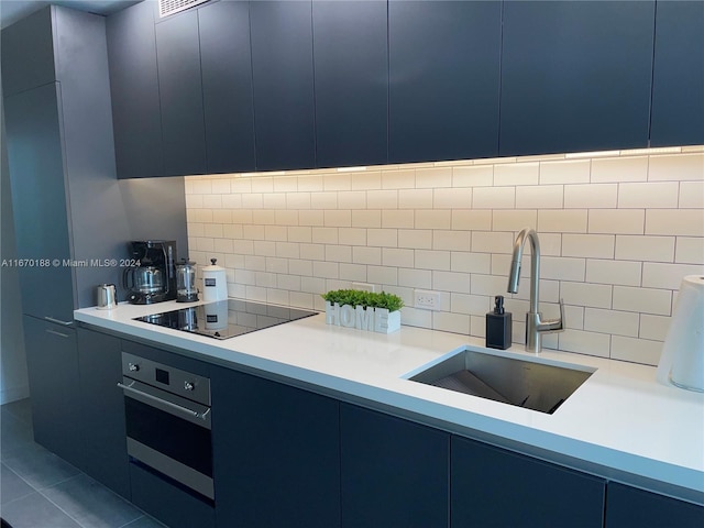 kitchen with sink, tasteful backsplash, oven, blue cabinetry, and black electric cooktop