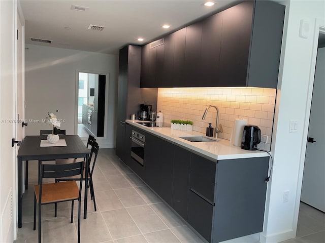 kitchen with light tile patterned flooring, sink, stainless steel oven, and tasteful backsplash