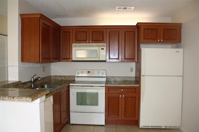 kitchen with a textured ceiling, sink, white appliances, light tile patterned floors, and dark stone countertops