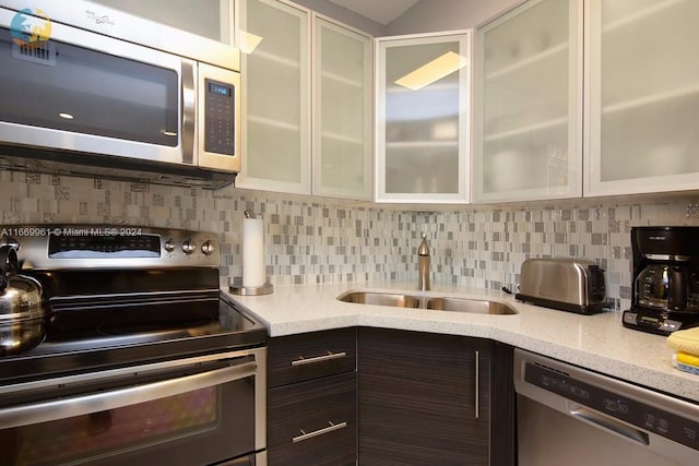 kitchen featuring dark brown cabinets, a sink, glass insert cabinets, backsplash, and appliances with stainless steel finishes