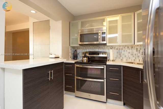 kitchen featuring dark brown cabinets, decorative backsplash, glass insert cabinets, and appliances with stainless steel finishes