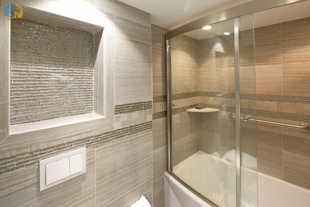 bathroom featuring bath / shower combo with glass door and tile walls