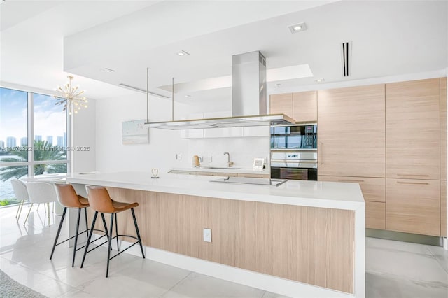 kitchen with a large island, island range hood, light brown cabinetry, light tile patterned floors, and black appliances