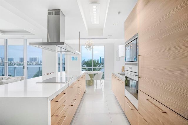 kitchen featuring a large island, light brown cabinets, wall oven, island range hood, and light tile patterned flooring