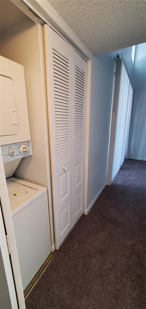 215 Lake Pointe Dr Unit 210, Oakland Park, FL 33309 - laundry room with a textured ceiling, carpet, baseboards, laundry area, and stacked washer and dryer