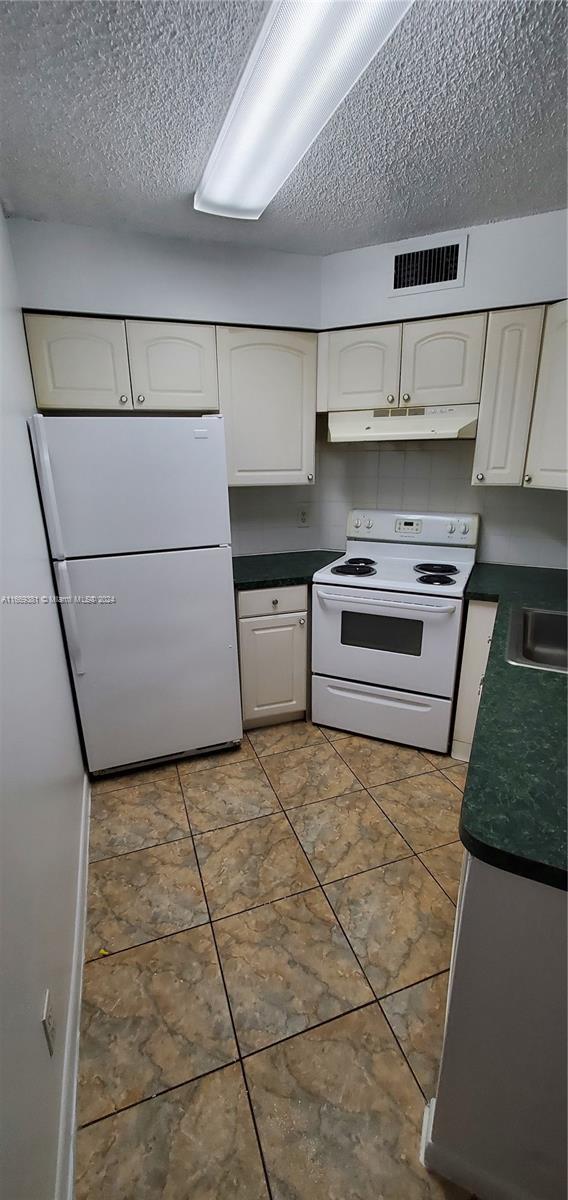 215 Lake Pointe Dr Unit 210, Oakland Park, FL 33309 - kitchen with visible vents, dark countertops, under cabinet range hood, and white appliances