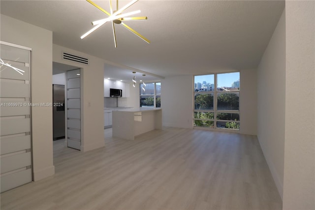 unfurnished living room featuring light wood-type flooring, a chandelier, and a textured ceiling