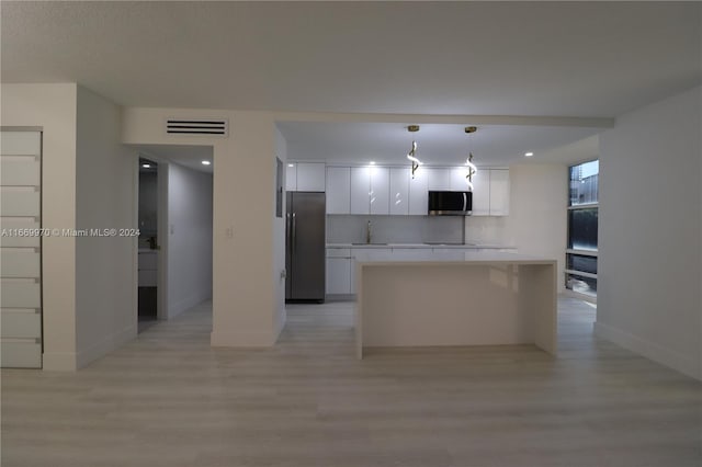 kitchen featuring white cabinetry, stainless steel appliances, light wood-type flooring, a center island, and decorative light fixtures