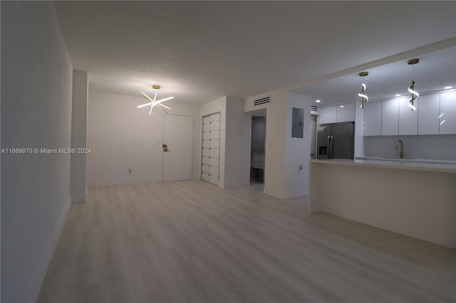 unfurnished living room with electric panel, sink, light hardwood / wood-style flooring, and a chandelier