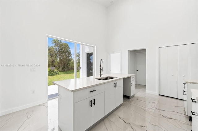 kitchen featuring an island with sink, a high ceiling, white cabinets, and sink