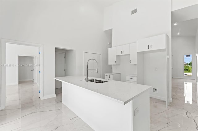 kitchen featuring a center island with sink, white cabinetry, a towering ceiling, and sink