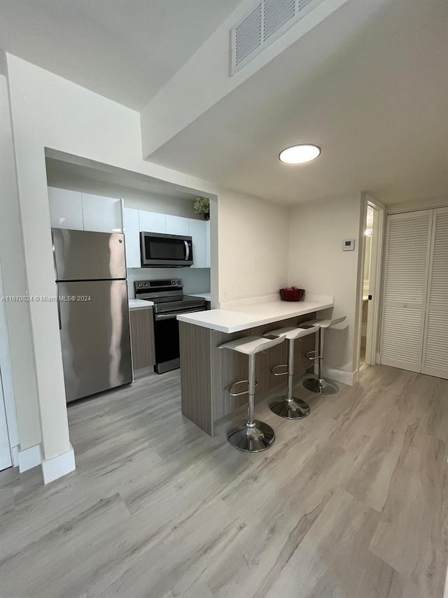 kitchen featuring white cabinetry, kitchen peninsula, stainless steel appliances, a kitchen bar, and light hardwood / wood-style flooring