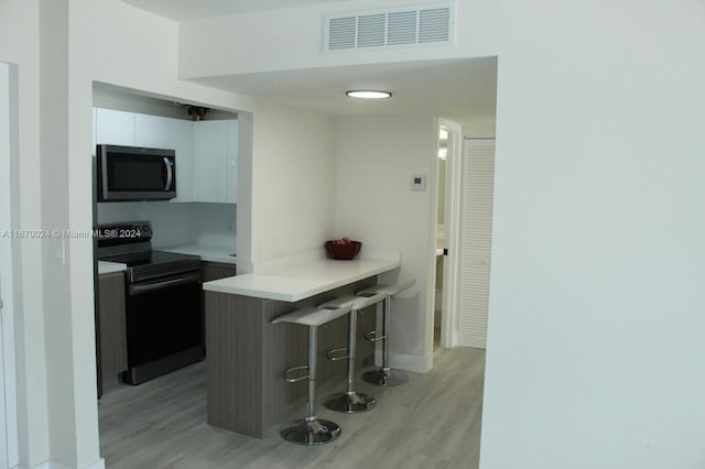 kitchen with a kitchen breakfast bar, white cabinets, kitchen peninsula, black range with electric cooktop, and light hardwood / wood-style flooring