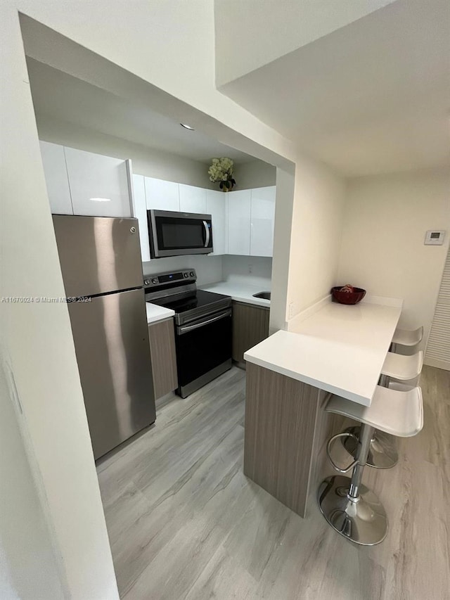 kitchen featuring appliances with stainless steel finishes, white cabinetry, a kitchen breakfast bar, and light hardwood / wood-style flooring