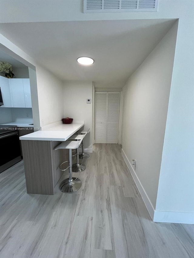 kitchen with a kitchen breakfast bar, kitchen peninsula, light wood-type flooring, and white cabinets