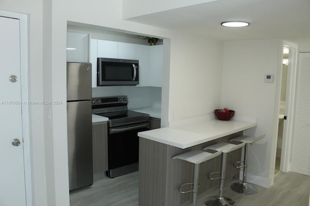 kitchen with kitchen peninsula, a kitchen bar, white cabinetry, appliances with stainless steel finishes, and light hardwood / wood-style floors