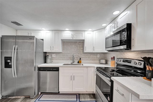 kitchen featuring sink, backsplash, white cabinetry, stainless steel appliances, and hardwood / wood-style floors